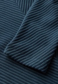 Teal ribattuj tissus med en strukturert finish, med en foldet kant som avslører de distinkte vertikale stripene i et mykt, strikket materiale.