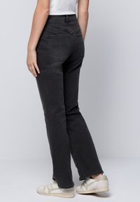 Zwarte denim jeans met een recht model, voorzien van achterzakken en subtiele stikdetails, gecombineerd met lichtgekleurde sneakers.