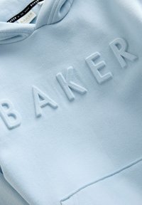 Hele sinine kapuutsiga särgiga, millel on reljeefne "BAKER" tekst, pehme tekstuur, kengurust tasku ja reguleeritav kapuuts nööriga.