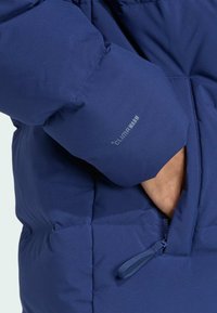 Tmavomodrá prešívaná bunda z textúrovaného materiálu, s logom ClimaWarm, vreckom na zips a elastickými manžetami pre lepšiu izoláciu.