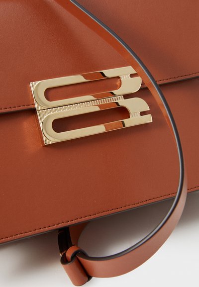 El bolso de cuero color tan presenta un destacado broche dorado con un diseño moderno, complementado por una correa delgada marrón.