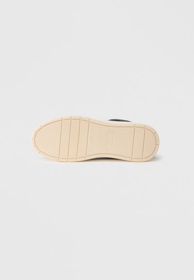 Μαύρο αθλητικό παπούτσι με υφαντό επάνω μέρος και εξωτερική σόλα από κρεμ χρώμα, με σχεδιασμένο πέλμα για πρόσφυση.