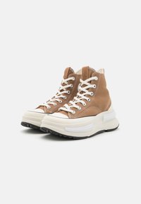 Braune Canvas-High-Top-Sneaker mit cremefarbenen Gummisohlen, weißen Schnürsenkeln und kontrastierenden Nähten. Enthält eine schwarze strukturierte Außensohle.