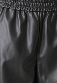 Svart lädertyg med en slät yta och sammanvikt midja. Materialet visar subtila variationer i ljus och skugga.