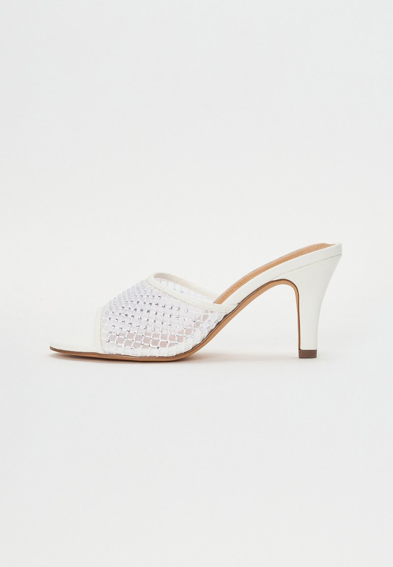 Mules de tacón blancos con parte superior de malla trenzada con acentos brillantes, diseño de punta abierta y suela de cuero suave con tacón afinado.