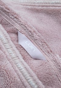 Rosa frottéfilt med mjuk textur, försedd med ett påsytt LUMIN LIVING-märke och en dragkedjekant. Detaljerad sömnad synlig längs sömmarna.