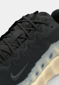 Adidași negri cu un design ondulat, superior texturat și șireturi închise la culoare. Talpa este translucidă, dezvăluind un model de grilă dedesubt.