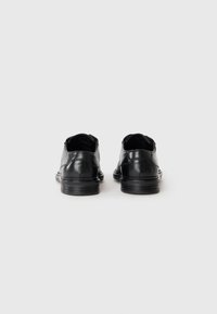 Par de zapatos de vestir de cuero negro vistos desde atrás sobre un fondo blanco liso.