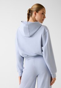 Felpa corta celeste con cappuccio regolabile e polsini a coste, abbinata a pantaloni celesti coordinati, caratterizzati da una texture liscia e morbida.