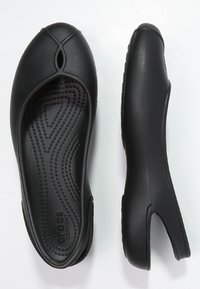 Chaussures noires à enfiler, flexibles, avec un design à découpes ovales. Semelles intérieures texturées avec des motifs en vagues. Fini doux et mat. Construction légère.