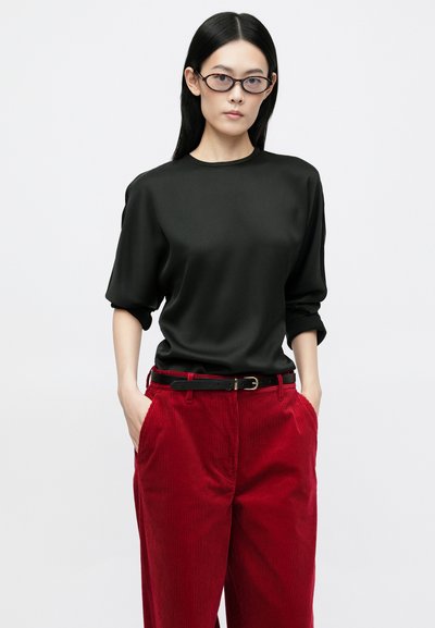 Black, short-sleeve top made of smooth fabric, paired with red corduroy pants featuring side pockets and a black belt.