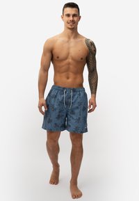Blauwe zwemshorts met een palmbomenpatroon, elastische tailleband met trekkoord en een klein logoaccent. Geschikt voor strandkleding.