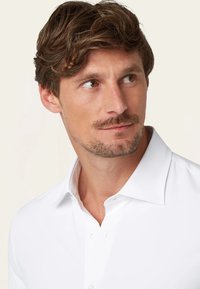 Weißes Hemd mit strukturiertem Kragen, glatter Textur und schlanker Passform. Der Stoff wirkt leicht und frisch.