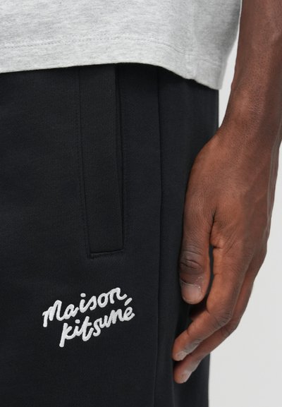 Pantaloni de trening negri cu o textură moale, având un logo brodat alb "Maison Kitsuné" pe lateral și un detaliu cu buzunar lateral.