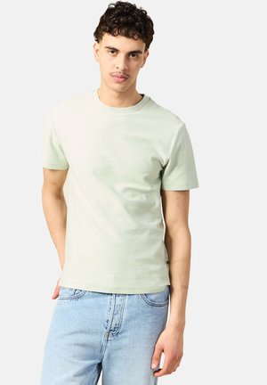 Lichtgroene t-shirt met korte mouwen van katoen, met een ronde halslijn en een ontspannen pasvorm. Draag het met lichtblauwe denim jeans.