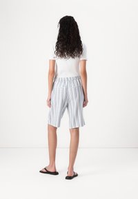 Un short bleu et blanc à rayures avec une taille élastique et deux poches arrière, associé à un haut blanc ajusté et des tongs noires.