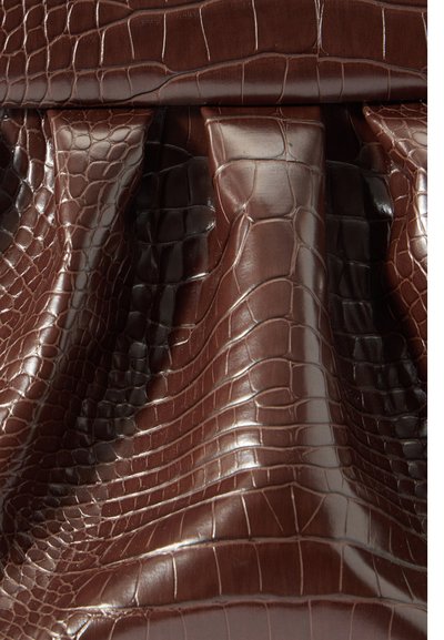 Close-up de couro castanho texturizado com padrão de crocodilo e detalhes dobrados criando sombras e realces.