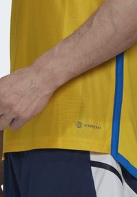 Camiseta deportiva amarilla con textura de malla, con acentos azules y el logo 'AEROREADY'. Manga corta y ajuste relajado.