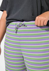 Spodnie w paski w kolorach zielonym, purpurowym i białym, z regulowanym pasem na sznurku oraz teksturą ściągacza. Casualowy design.