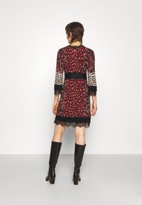 Punainen mekko, jossa leopardikuvioita ja kukkakuoseja, ohuet pitsikoristeet, 3/4-hihat, istuva vyötärö ja pitsireuna, yhdistetty polvimittaisten mustien saappaiden kanssa.