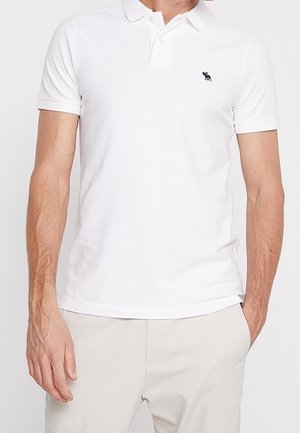Biała koszulka polo z krótkim rękawem, z zapięciem na trzy guziki i małym haftowanym logo po lewej stronie klatki piersiowej. Wykonana z miękkiej, strukturalnej tkaniny.