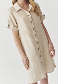 Abito button-up in lino beige con colletto, maniche corte arrotolate e bottoni in legno, caratterizzato da una vestibilità rilassata e un orlo curvo.