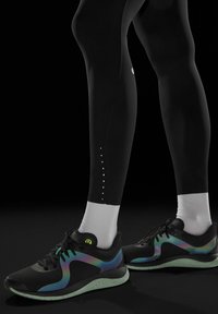 Czarne legginsy sportowe z odblaskowymi białymi kropkami; w połączeniu z czarnymi butami do biegania z irydyscencyjnymi akcentami i teksturowaną podeszwą.