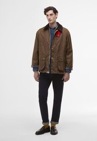 Brown, quilted jacket with a corduroy collar and red accent, featuring two front pockets, layered over a blue shirt and plaid flannel.
