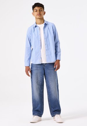 Lichtblauw gestreept overhemd met knopen over een wit T-shirt, gecombineerd met losse blauwe jeans en witte sneakers. Eenvoudig ontwerp, casual pasvorm.