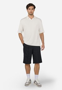 Short-sleeve, collared polo shirt in light cream, paired with dark navy shorts. Individual wears white socks and gray sneakers with beige accents.