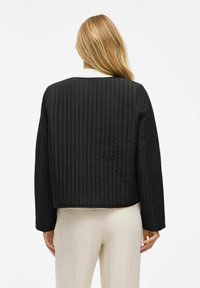 Svart quiltad jacka med en boxig design, som har långa ärmar och rund halsringning. Materialet har en slät textur och subtil sömnad.