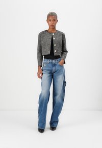 Sivá tweed skrátená bunda so štyrmi zlatými gombíkmi, spárovaná so svetlomodrými širokými džínsami. Čierne topánky dopĺňajú outfit, umiestnený na bielom pozadí.