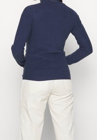 Marineblauer Langarmpullover mit hohem Kragen, aus weichem Stoff gefertigt, mit glatter Textur und tailliertem Design.