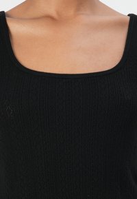 Svart strikket tanktop med firkantet hals, med et teksturert mønster av hevede diamanter og vertikale striper.