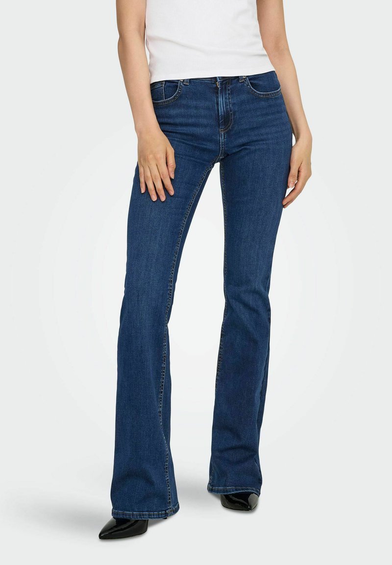 Ciemnoniebieskie dżinsowe spodnie dzwony. Posiadają pięć kieszeni, zamek z przodu oraz paski na pasek. Noszone z dopasowanym białym topem na ramiączkach.