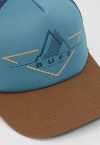 Traktoru cepure ar zilu auduma priekšpusi un brūnu teksturētu vizieri, kurā ir kalna grafika un "BUFF" logo tumši zilā krāsā ar vara akcentiem.