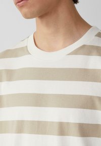 Beige en crème gestreepte kortemouwen t-shirt met een ronde geribbelde halslijn en zachte stoftextuur, met afwisselend brede en smalle strepen.
