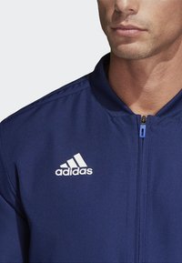 Navyblaue Zip-Jacke aus glattem Stoff mit Stehkragen und weißem Adidas-Logo auf der linken Brustseite.