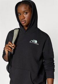 Μαύρο φούτερ με κουκούλα που διαθέτει μπροστινή τσέπη και πράσινο λογότυπο της The North Face. Το υλικό είναι μαλακό με άνετη εφαρμογή, σχεδιασμένο με κουκούλα.