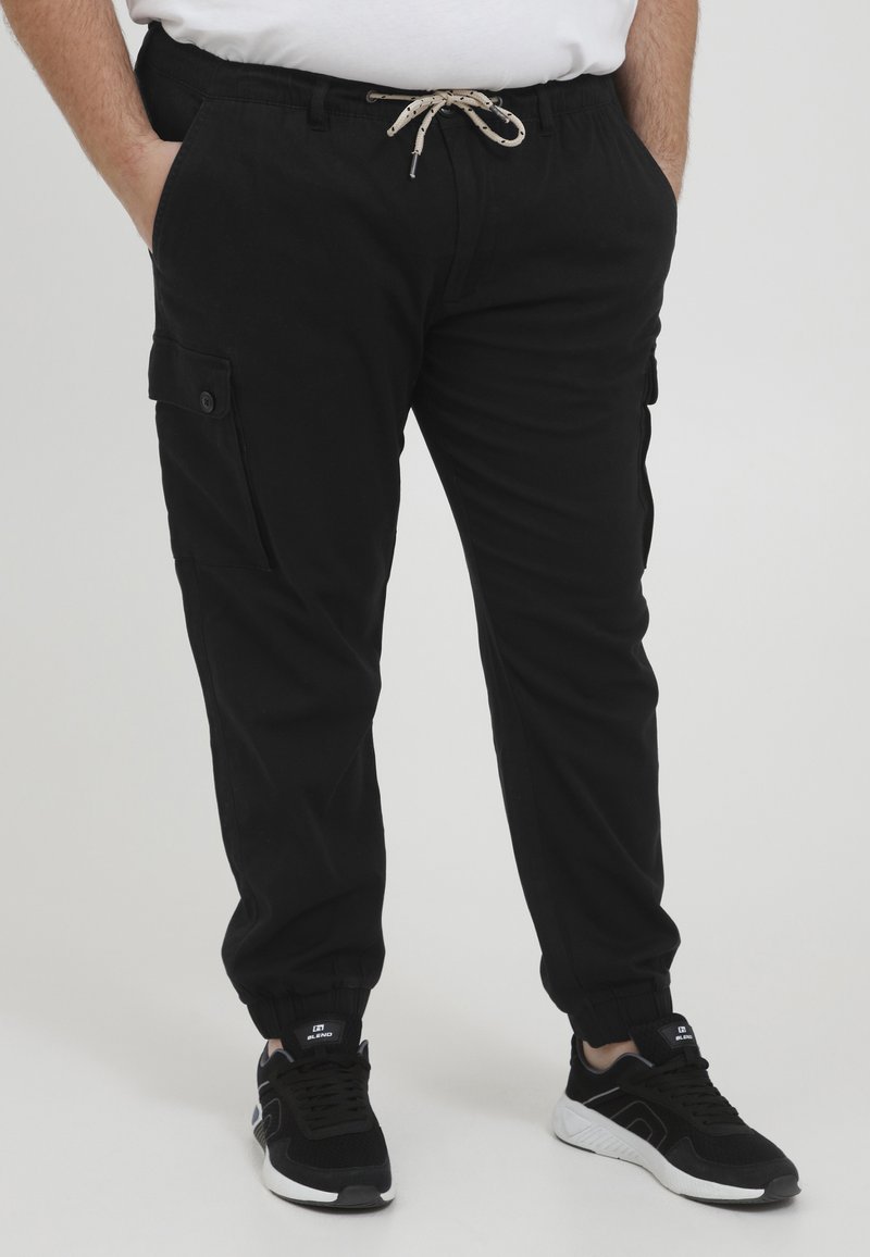 Schwarze Cargo-Hosen mit elastischem Bund, Kordelzug und seitlichen Taschen, ausgestattet mit elastischen Bündchen und einer glatten, matten Stofftextur.
