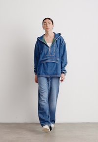 Jeanspullover med dragkedja längst fram, huva och framficka. Lösa jeansbyxor. Färg: blå med en grön accent under huvan.