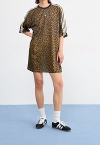 Löparmönstrad klänning med korta ärmar, svart krage, tre vita ränder på axlarna, kombinerad med svarta sneakers och vita strumpor.