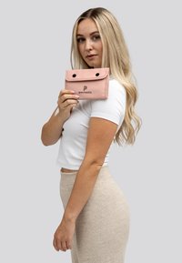 Roze stoffen portemonnee met een klep sluiting, twee zwarte drukknoopjes en een zwart logo. Gladde textuur en rechthoekige vorm.