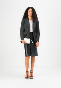 Blazer doppiopetto a righe nere, top lilla, gonna midi in pelle nera con spacco, borsa a pochette bianca e decollete neri con cinturini.