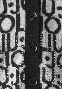 Cardigan in bianco e nero con motivo a fantasia, caratterizzato da una texture lavorata a maglia, con paillettes decorative e cinque bottoni sul davanti.