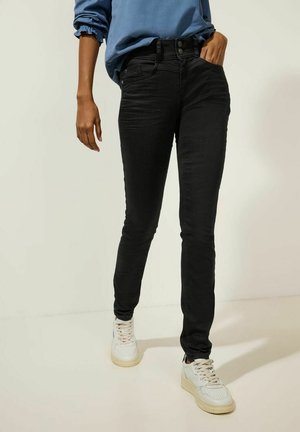 Jean skinny noir en denim, avec une taille haute, deux poches latérales et deux poches arrière, associés à des baskets blanches.