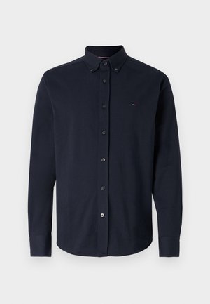 Camicia button-up blu navy a maniche lunghe. Materiale in cotone, colletto button-down e un piccolo logo sul lato sinistro del petto. Tessuto liscio, vestibilità standard.