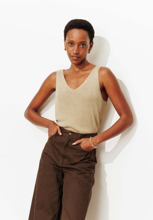 Débardeur en maille beige avec un col en V, associé à un pantalon large taille haute couleur brun foncé. Accent minimaliste avec un bracelet chaîne en or.