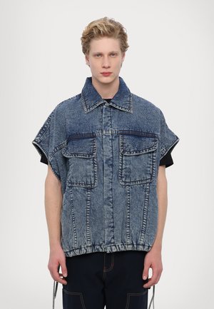 Lühikeste varukatega denimist overshirt, millel on kaks suurt eesmist taskut, nööbi sulgemine ja kogutud äärega. Kantud musta toppi peal.