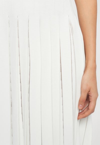 White pleated dress featuring vertical ribbed texture and metallic thread accents. Close-up view of the fabric and hand holding a pleat.